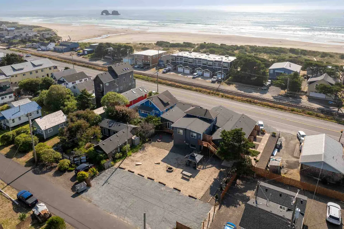 The image showcases a row of charming cottages just steps from the sandy shoreline, with the sparkling ocean stretching beyond, a quiet road separating the homes from the inviting beach. The scene hints at families enjoying beachcombing, gentle strolls along the shore, and the welcoming atmosphere of a small coastal community.