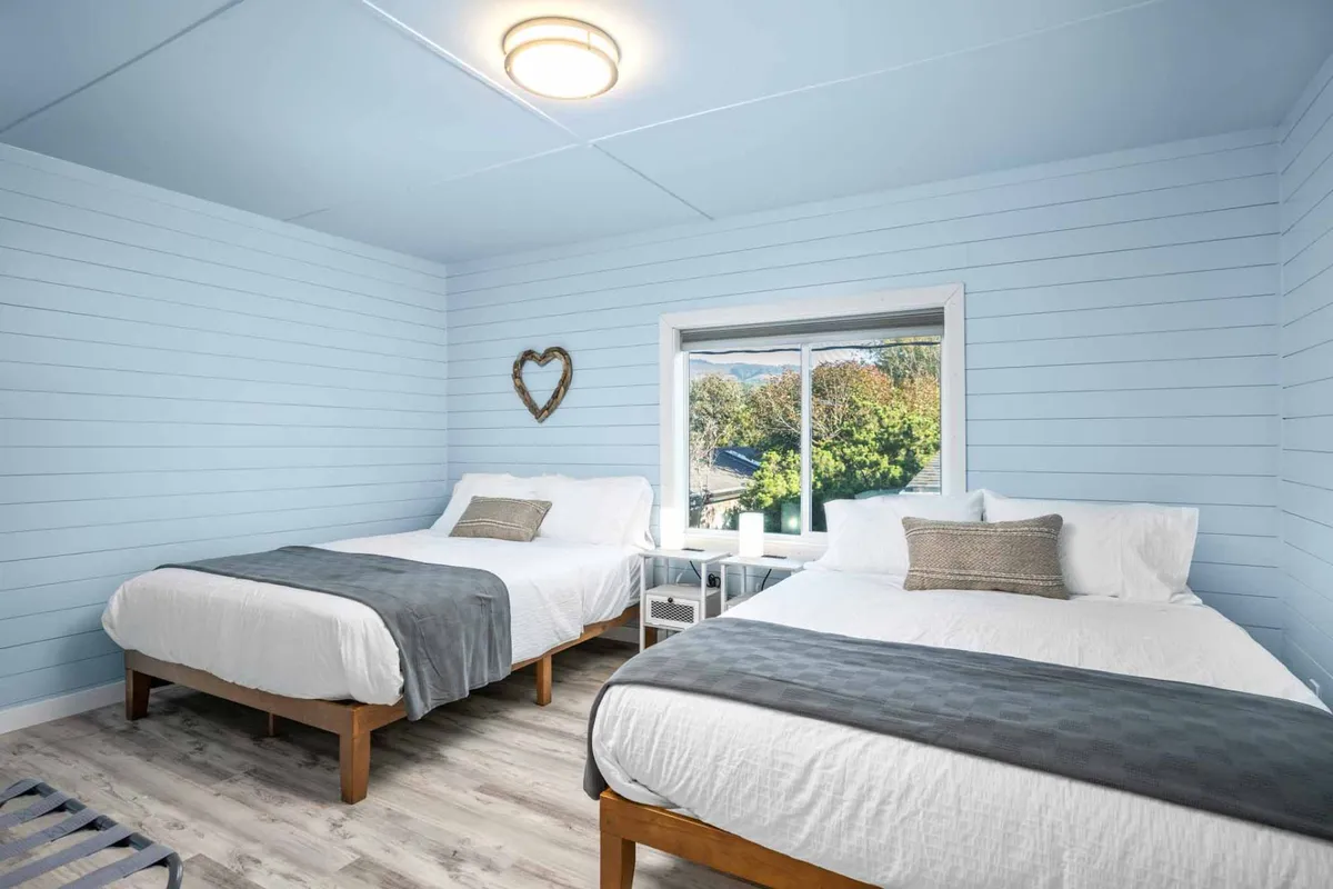A tranquil sleeping area with two beds, a window offering a peaceful view, and heart-shaped decor. Daylight fills the room, creating a serene and cozy retreat for rest and relaxation.