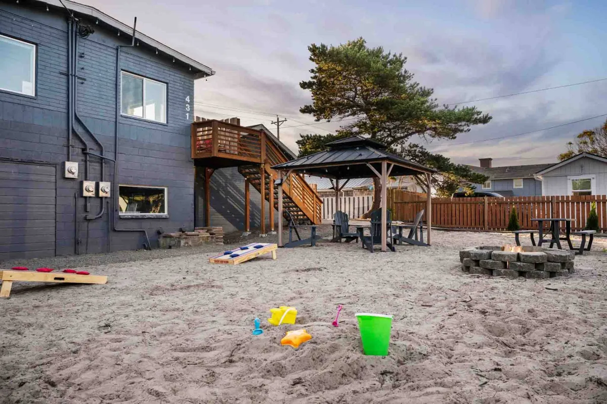 A vibrant outdoor scene featuring a gazebo, outdoor seating, a sandbox, and a cornhole game. The area is lively and welcoming, encouraging both relaxation and social activities. The gazebo is the focal point, surrounded by communal amenities that invite guests to mingle and share experiences.