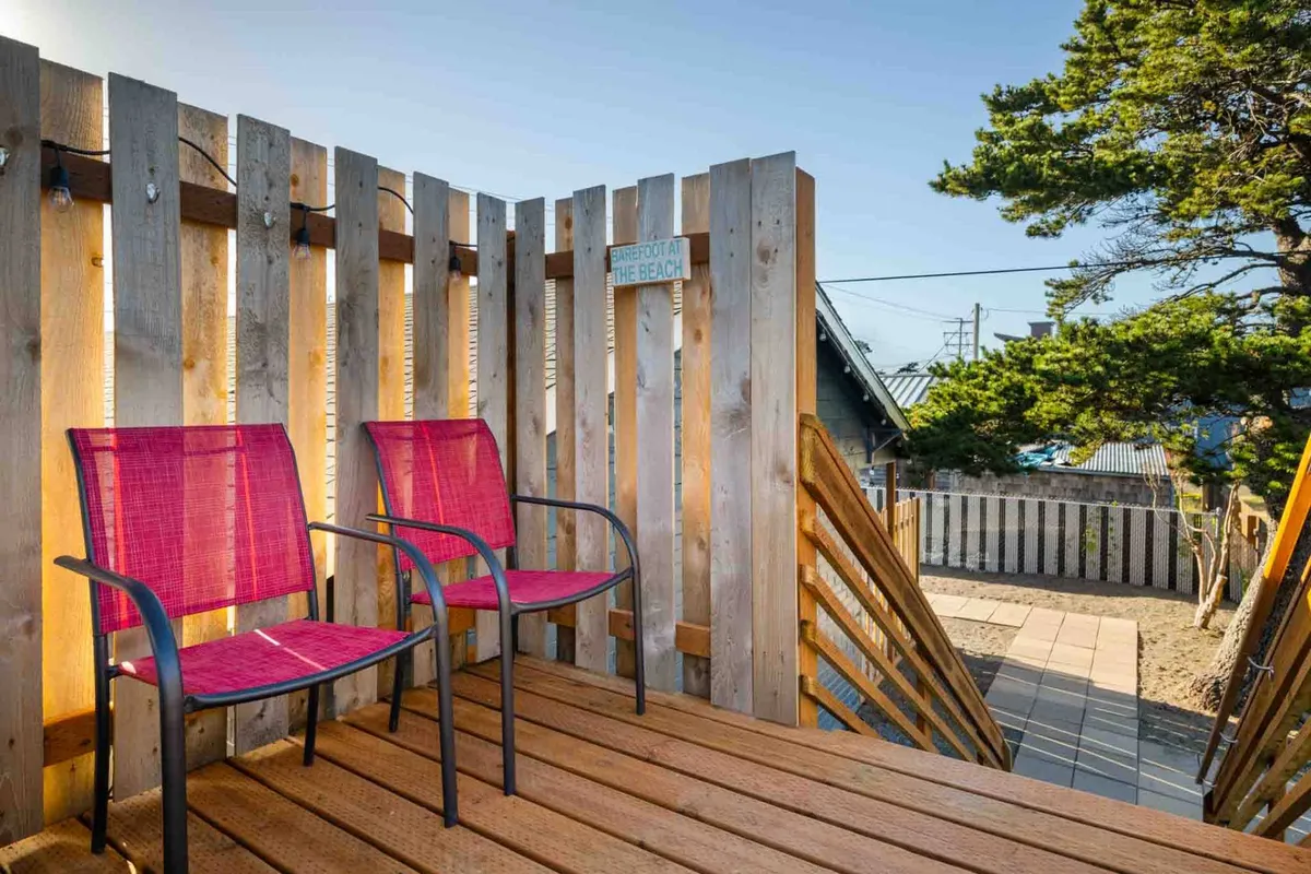 This image showcases a cozy wooden deck with two inviting red chairs, a wooden fence, and a small signboard. The scene is tranquil, suggesting a space for quiet relaxation, perhaps while enjoying morning coffee or an evening drink. The layout provides a clear sense of a private patio area that feels both welcoming and personal.