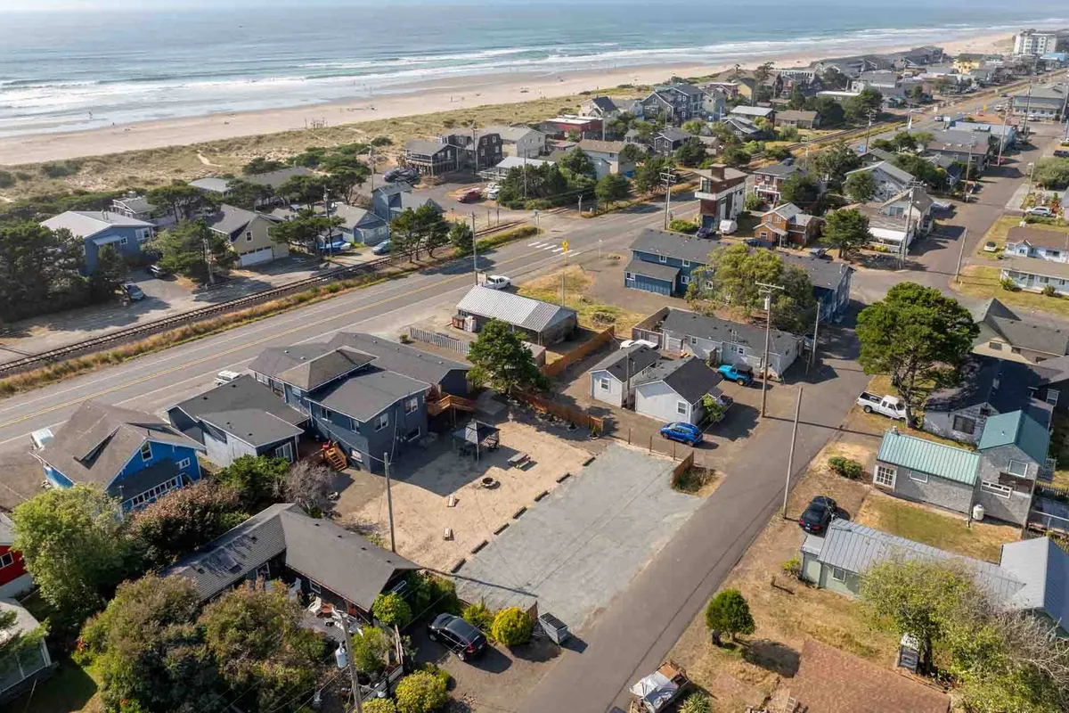 A captivating exterior shot showing beachfront homes, the ocean, a tree-lined road, and the continuous stretch of sandy beach. The road draws the eye toward the shoreline, reinforcing both the accessibility and the scenic beauty of the neighborhood.