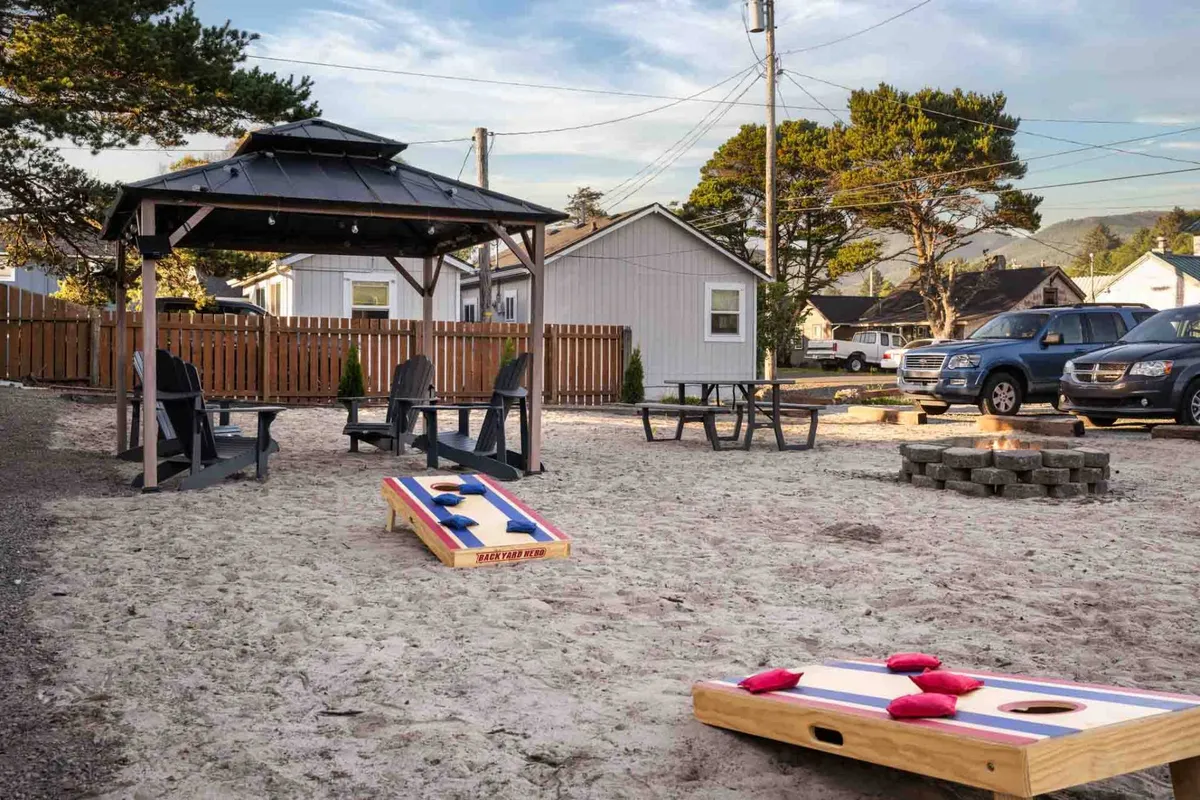 An inviting communal outdoor space featuring a gazebo, cornhole game, fire pit, and ample seating. The area is designed for guests to gather, relax, and enjoy time together after a day at the beach.