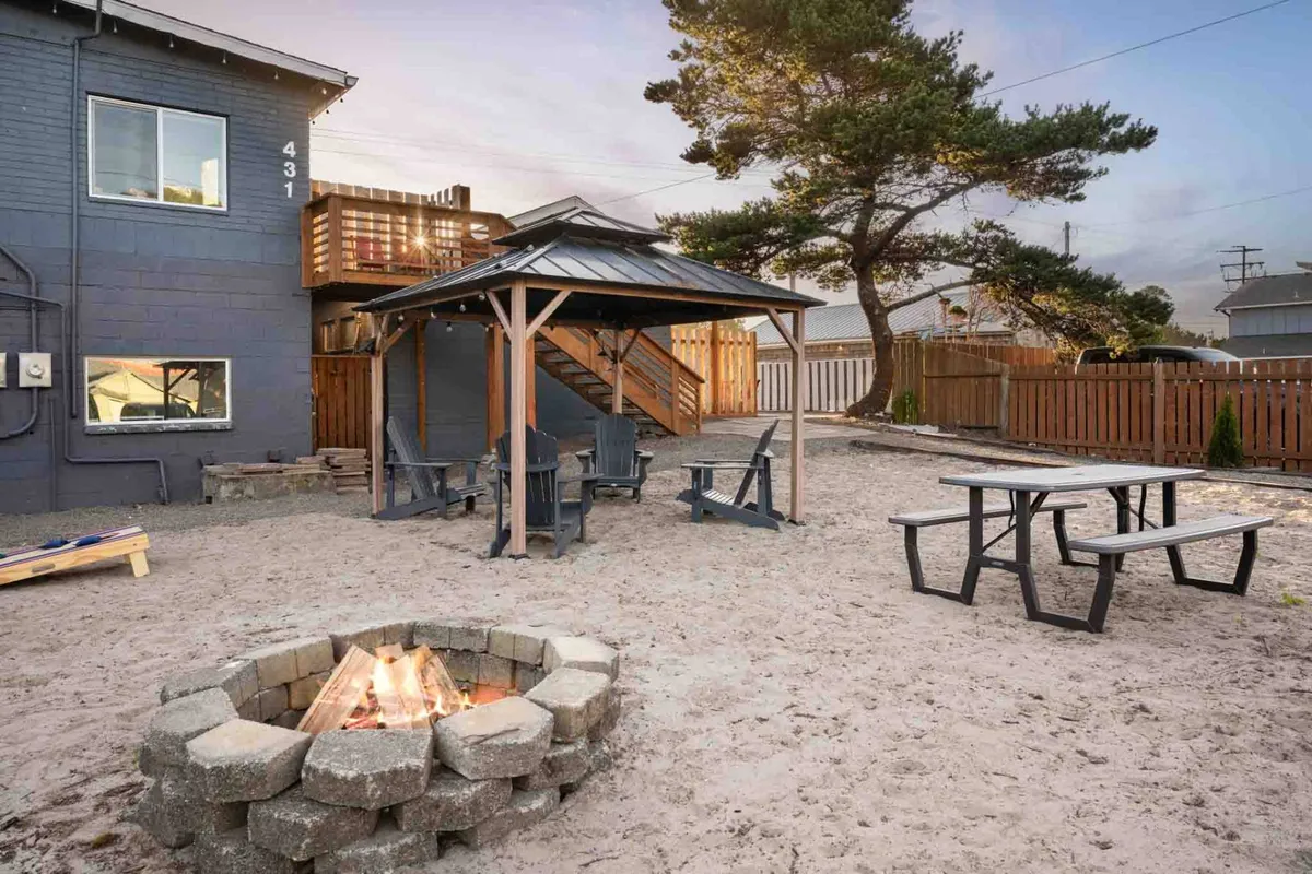 This image depicts a cozy fire pit surrounded by outdoor seating, a gazebo, and a staircase leading to an upper deck. The scene exudes a sense of warmth and gathering, showcasing an environment suited for group conversations, celebrations, or relaxing by the fire under the stars.