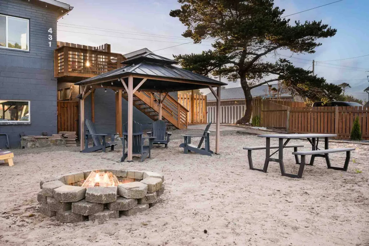 An inviting exterior scene featuring a cozy fire pit, gazebo, and comfortable outdoor seating area. The setting is surrounded by greenery and offers ample space for relaxing outdoors or taking a quick walk with your pet. The atmosphere suggests a communal and pet-friendly environment where guests can spend time outside with their pets.