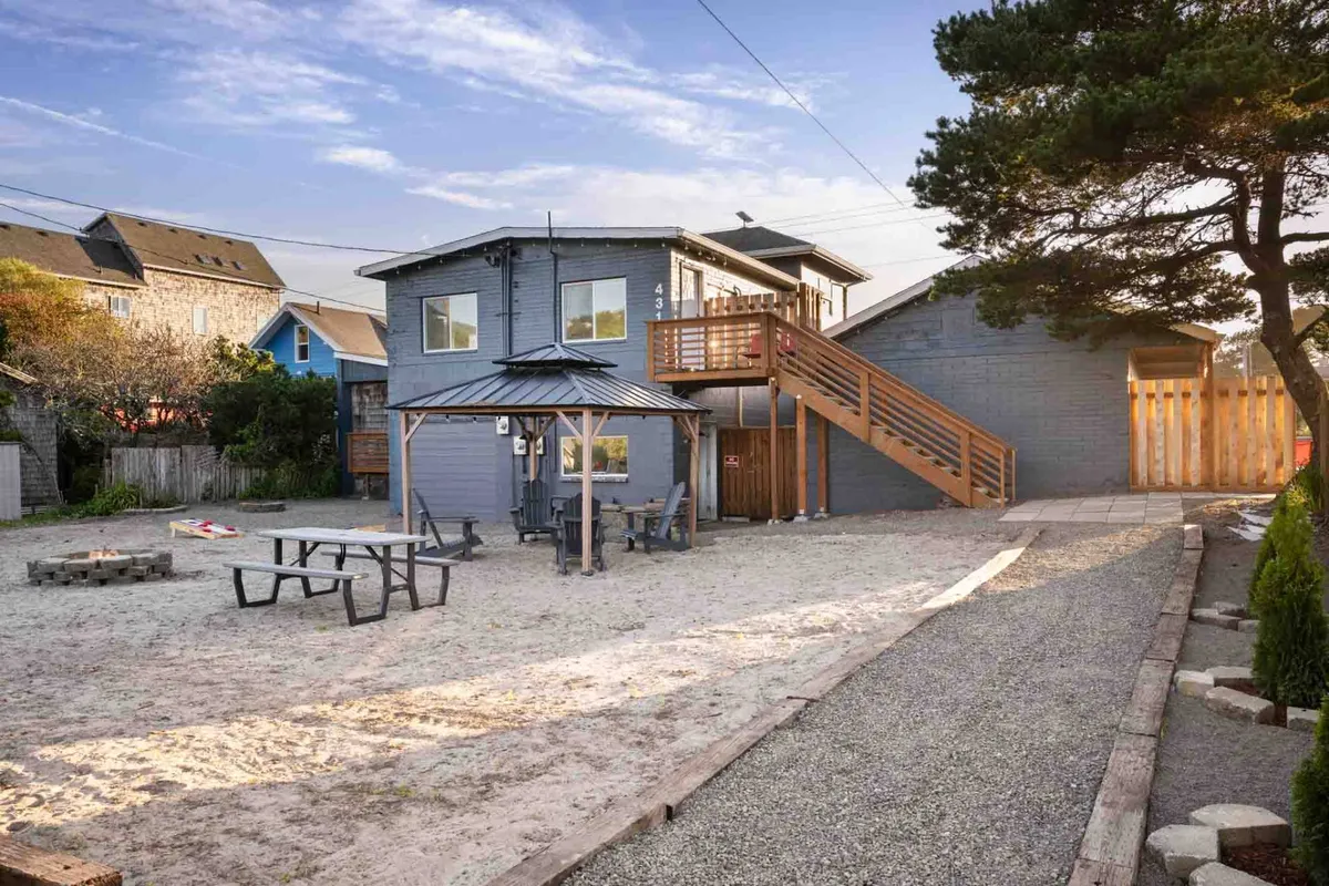 A two-story cottage with a large deck, sandy courtyard, picnic tables, and a fire pit. The outdoor setting feels casual and friendly—ideal for sunset dining, campfire storytelling, and stargazing on clear nights.