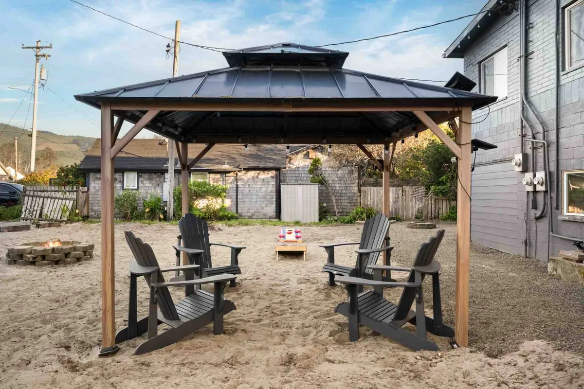 An inviting exterior communal area with a gazebo, Adirondack chairs, and a fire pit, set against a backdrop of natural greenery. This space is perfect for relaxing or gathering with friends after a day of sightseeing.