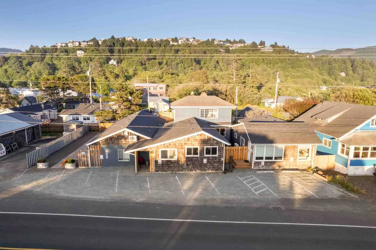 An exterior shot of the main building, clad in wooden shingles, with a welcoming porch, surrounded by greenery and a hillside. The scene suggests a peaceful retreat close to nature, with spots to relax outdoors.